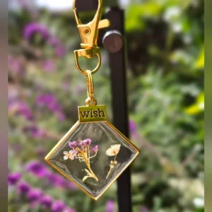 Gold bag charm with a lobster claw clasp featuring a delicate pressed flower encased in clear epoxy resin