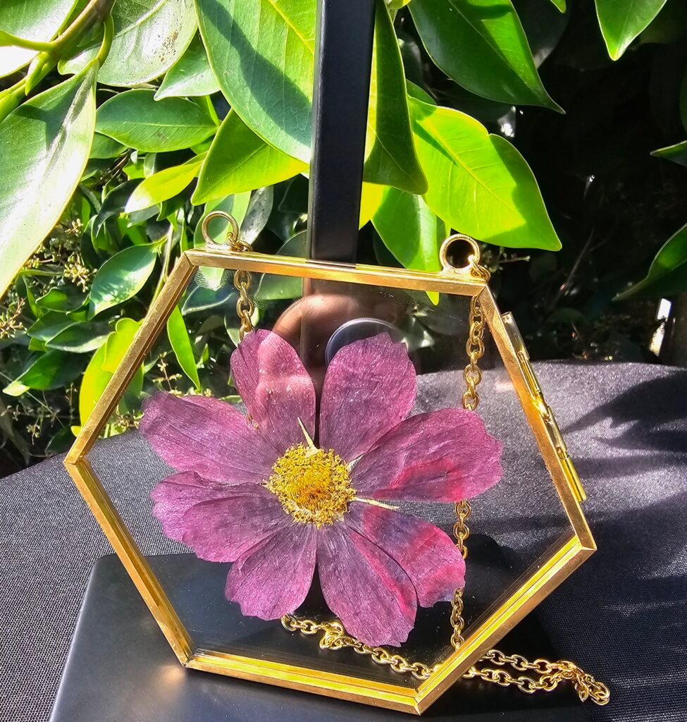 Fresh purple pressed flower encased in a glass picture frame with gold-colored metal edges.